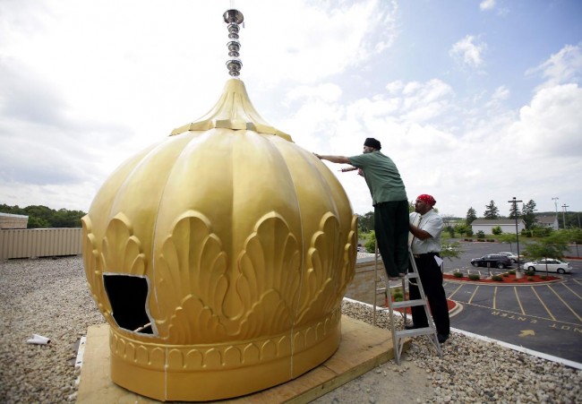 Harcharan Gill (right), a trustee and public relations committee member for the Sikh temple holds up temple member Balwinder Singh as they work on caulking the seams of a dome. - Image credit: Mike De Sisti 