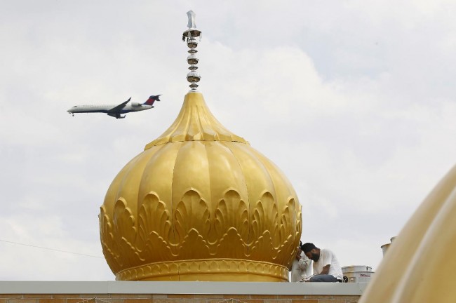 An airplane flies overhead as Jaspreet Singh works installing one of seven domes. - Image credit: Mike De Sisti 