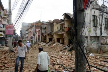 Nepalese people walk past collapsed buildings at Lalitpur, on the outskirts of Kathmandu on April 25, 2015.  A powerful 7.9 magnitude earthquake struck Nepal, causing massive damage in the capital Kathmandu with strong tremors felt across neighbouring countries.  